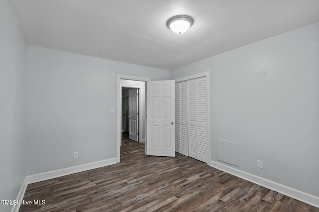 unfurnished bedroom featuring dark wood-type flooring, a closet, and baseboards