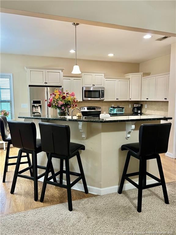 kitchen with stainless steel appliances, a kitchen island with sink, white cabinets, and a kitchen breakfast bar