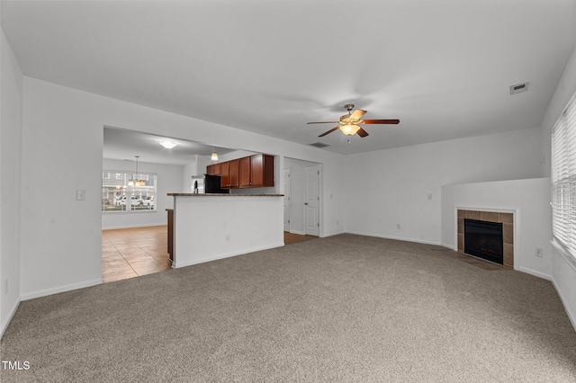 unfurnished living room featuring visible vents, a tiled fireplace, a ceiling fan, light carpet, and baseboards