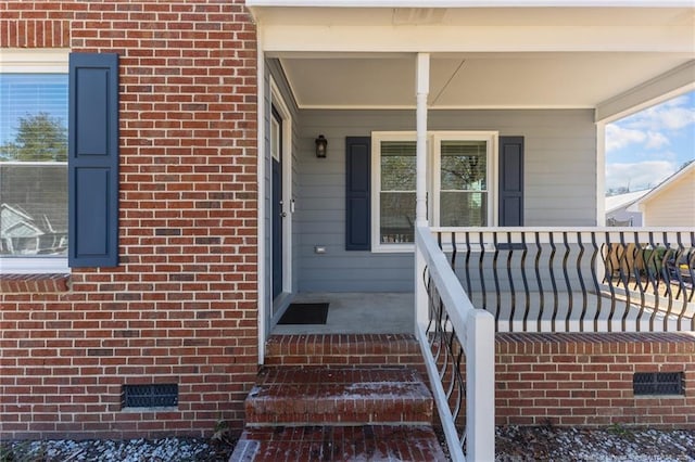 entrance to property with covered porch, brick siding, and crawl space