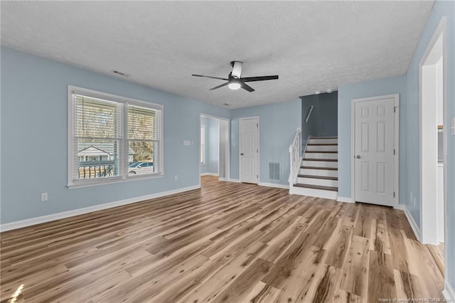 unfurnished living room featuring light wood-type flooring, visible vents, a textured ceiling, and stairs