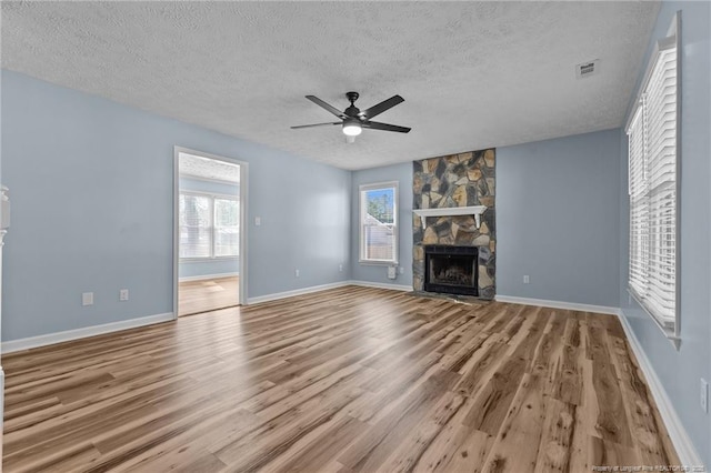 unfurnished living room featuring a textured ceiling, a stone fireplace, light wood-style flooring, visible vents, and a ceiling fan