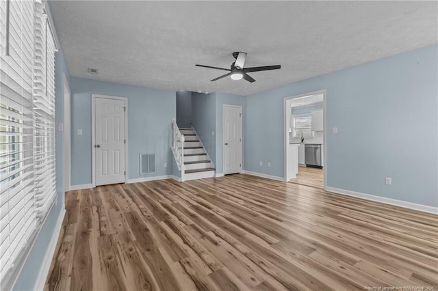 unfurnished living room featuring visible vents, light wood-style floors, a ceiling fan, baseboards, and stairs