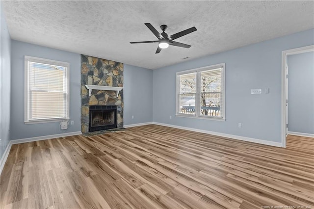 unfurnished living room featuring a textured ceiling, a stone fireplace, a ceiling fan, baseboards, and light wood-style floors