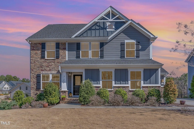 craftsman house featuring stone siding, a front lawn, board and batten siding, and roof with shingles