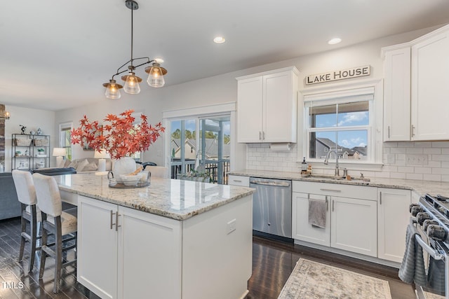 kitchen with white cabinets, appliances with stainless steel finishes, open floor plan, a center island, and a sink