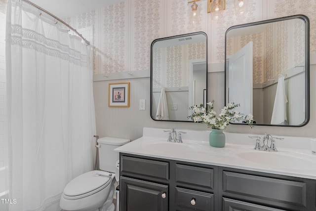 full bathroom with double vanity, a sink, toilet, and wallpapered walls