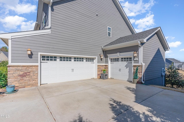 view of side of home with a garage, stone siding, and driveway