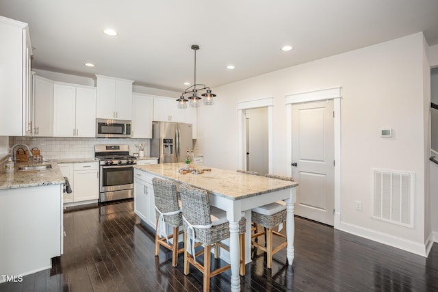 kitchen with visible vents, a sink, stainless steel appliances, decorative backsplash, and dark wood-style floors