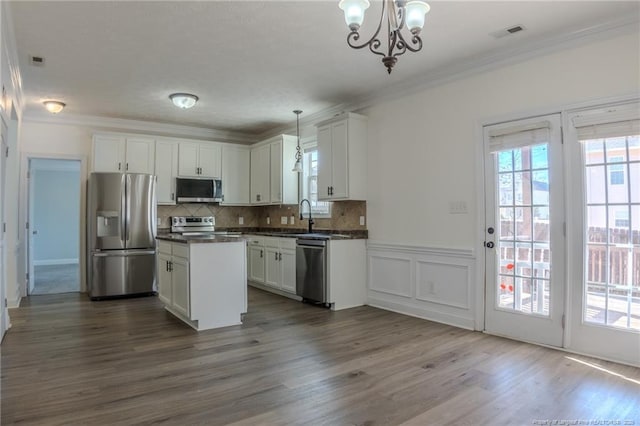 kitchen with dark countertops, appliances with stainless steel finishes, crown molding, white cabinetry, and pendant lighting