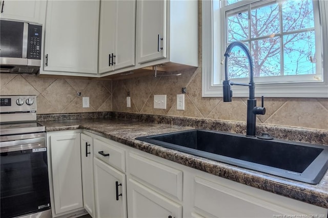 kitchen featuring stainless steel appliances, dark countertops, white cabinets, and a sink