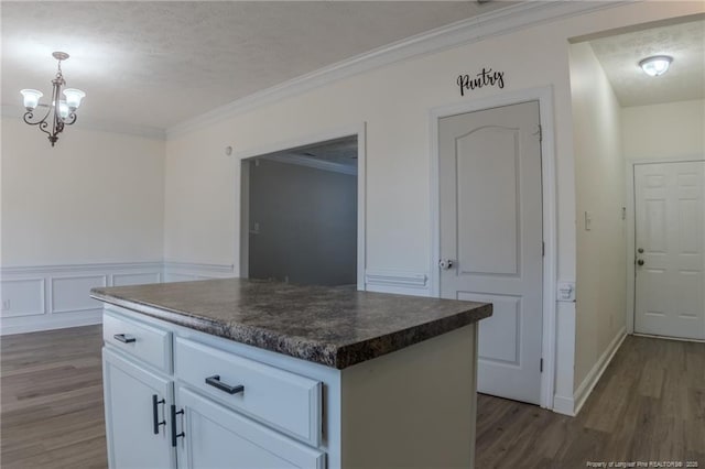 kitchen featuring white cabinets, a center island, dark countertops, dark wood finished floors, and crown molding