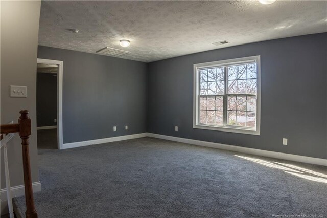 spare room featuring a textured ceiling, dark carpet, visible vents, and baseboards