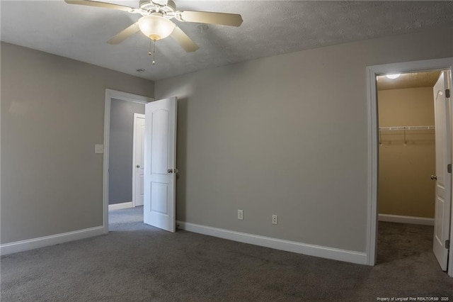 unfurnished bedroom with a walk in closet, baseboards, and dark colored carpet