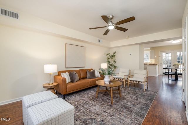 living area featuring dark wood-type flooring, visible vents, baseboards, and a ceiling fan