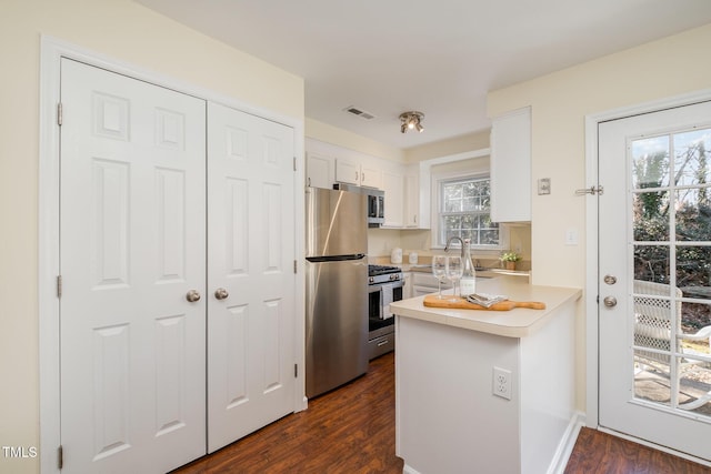 kitchen featuring dark wood-style floors, a peninsula, stainless steel appliances, light countertops, and white cabinetry