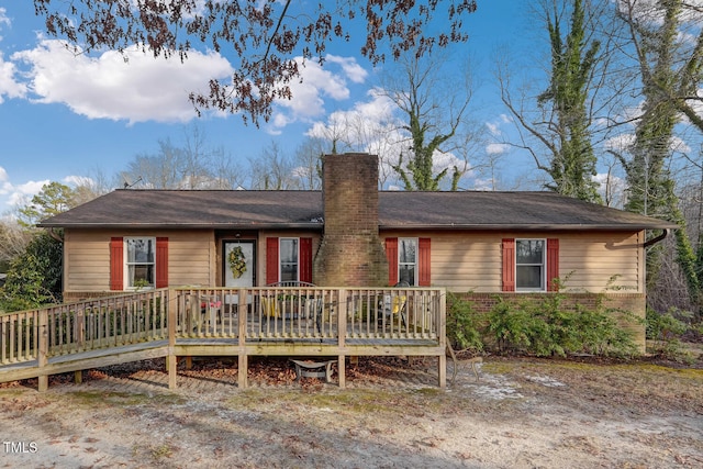 ranch-style home with brick siding, a chimney, and a wooden deck