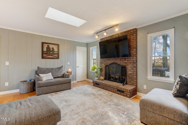 living area featuring a skylight, a brick fireplace, wood finished floors, and crown molding