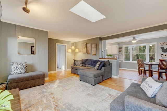 living room featuring a skylight, light wood-style flooring, ornamental molding, and a textured ceiling