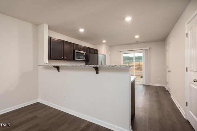 kitchen featuring stainless steel appliances, baseboards, a kitchen breakfast bar, dark brown cabinets, and dark wood-style floors