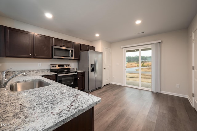 kitchen with light stone counters, a sink, dark brown cabinets, appliances with stainless steel finishes, and dark wood-style floors