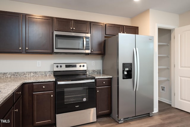 kitchen with light stone countertops, appliances with stainless steel finishes, dark brown cabinets, and wood finished floors