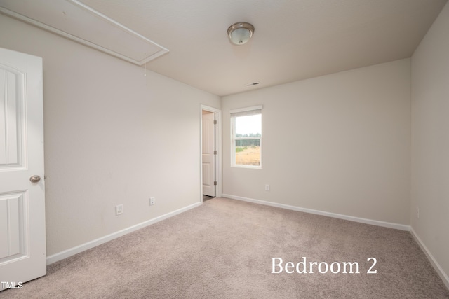 carpeted spare room with visible vents, attic access, and baseboards