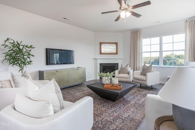 living area with baseboards, visible vents, a glass covered fireplace, ceiling fan, and dark wood-type flooring