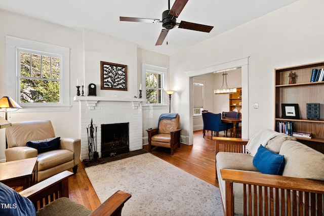 living room featuring a brick fireplace, wood finished floors, and ceiling fan