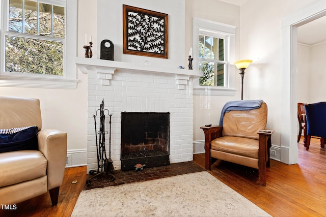 living area with plenty of natural light, a brick fireplace, and wood finished floors