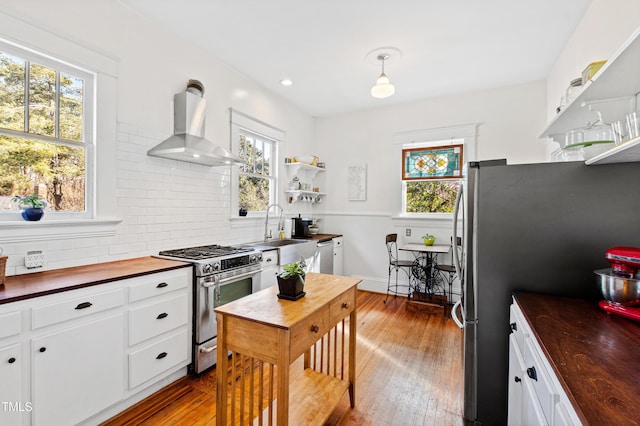 kitchen with a sink, butcher block countertops, stainless steel appliances, wall chimney exhaust hood, and tasteful backsplash