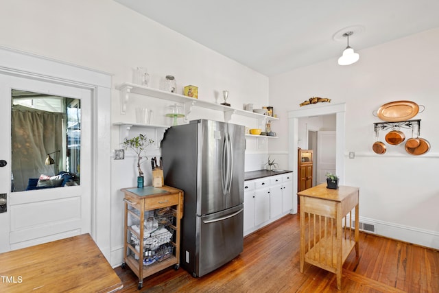 kitchen featuring visible vents, open shelves, freestanding refrigerator, wood-type flooring, and dark countertops