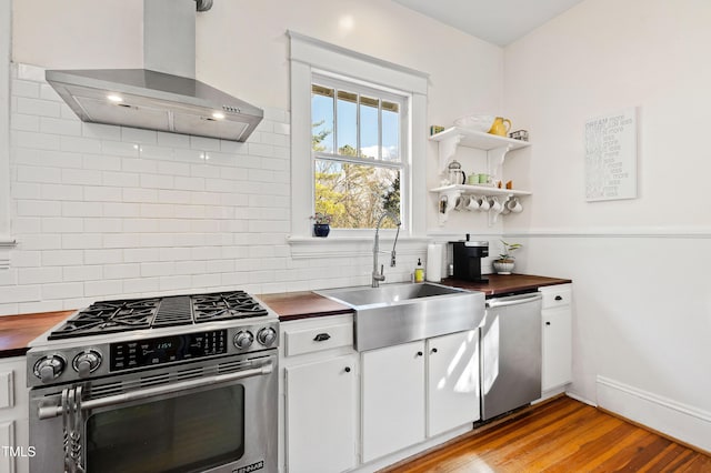 kitchen with wall chimney range hood, decorative backsplash, stainless steel appliances, wood counters, and a sink