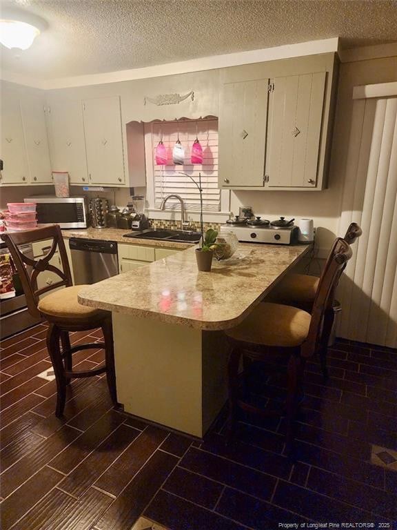 kitchen with appliances with stainless steel finishes, a peninsula, wood tiled floor, a textured ceiling, and a sink