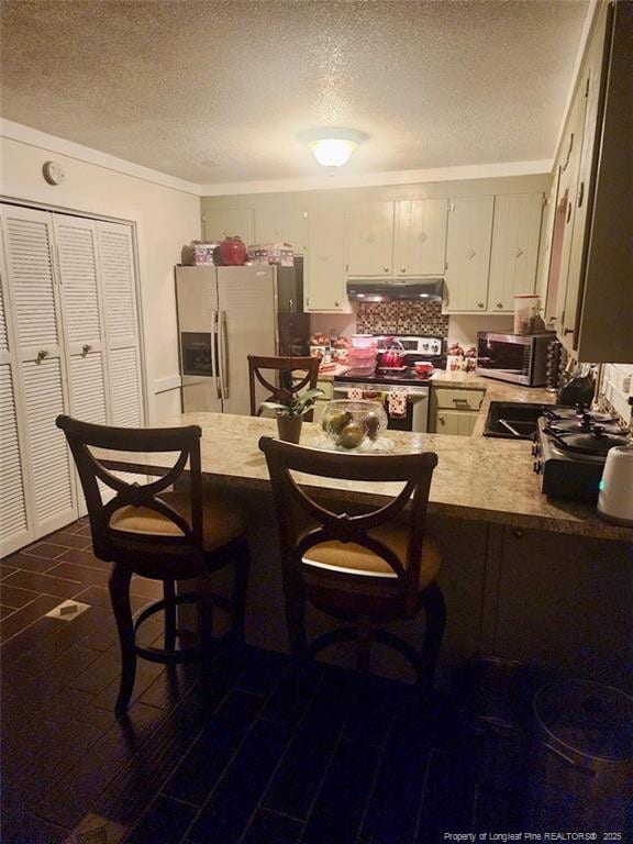 kitchen with appliances with stainless steel finishes, a peninsula, light countertops, under cabinet range hood, and a sink