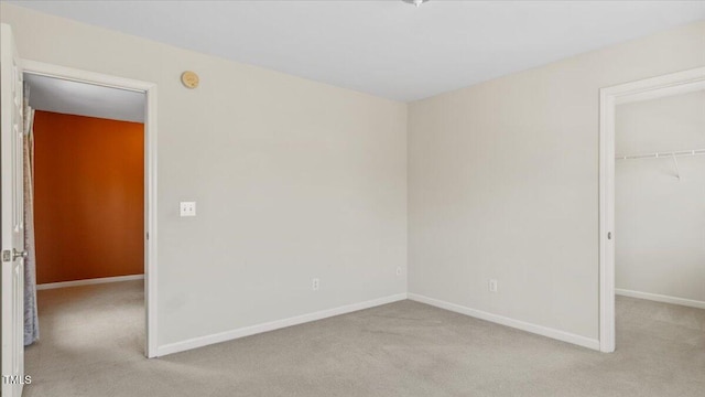 unfurnished bedroom featuring light carpet, baseboards, a walk in closet, and a closet