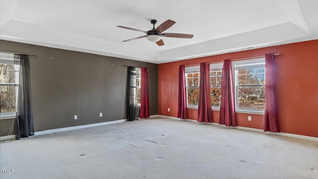 spare room with a tray ceiling, light colored carpet, plenty of natural light, and baseboards