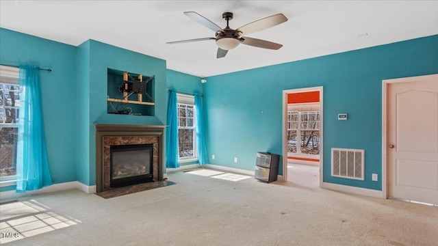 unfurnished living room featuring a healthy amount of sunlight, visible vents, light carpet, and a premium fireplace