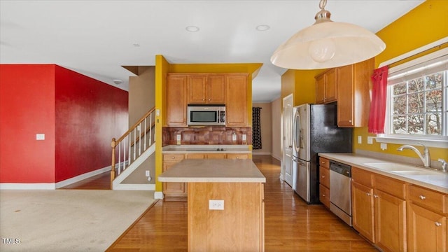 kitchen with appliances with stainless steel finishes, light countertops, a kitchen island, and hanging light fixtures