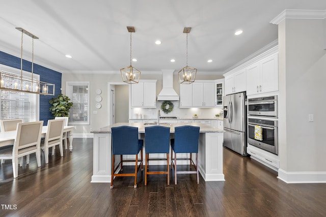 kitchen with crown molding, stainless steel appliances, custom range hood, an inviting chandelier, and an island with sink