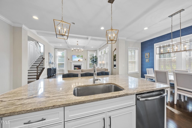 kitchen with a notable chandelier, stainless steel dishwasher, open floor plan, a sink, and a lit fireplace