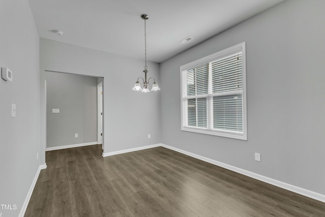 empty room with a chandelier, dark wood finished floors, and baseboards