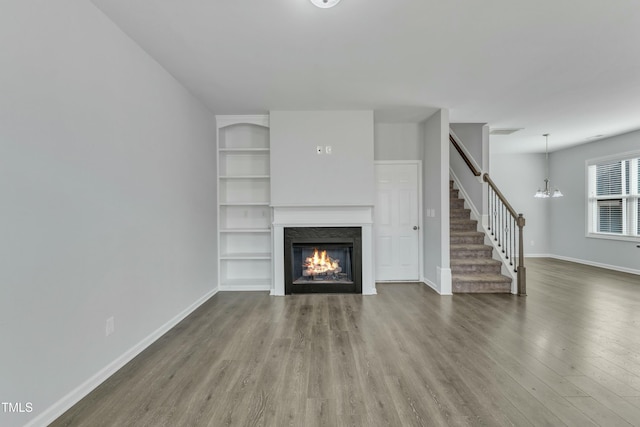 unfurnished living room featuring built in features, stairway, wood finished floors, a lit fireplace, and baseboards