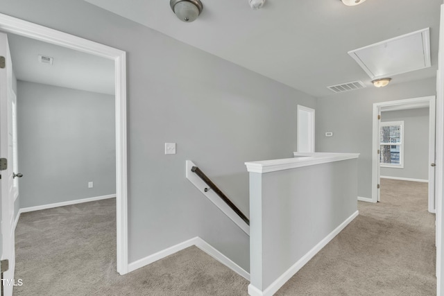 hall featuring carpet floors, visible vents, baseboards, an upstairs landing, and attic access