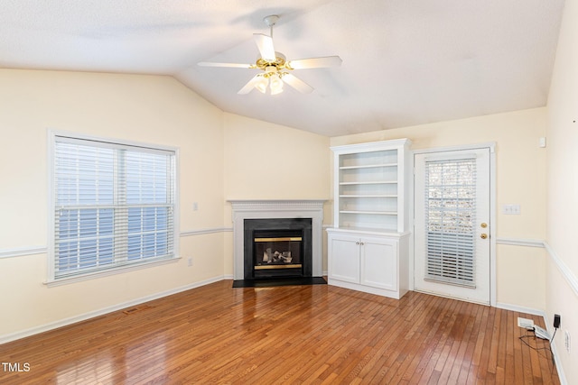 unfurnished living room with lofted ceiling, a fireplace with flush hearth, ceiling fan, wood finished floors, and baseboards