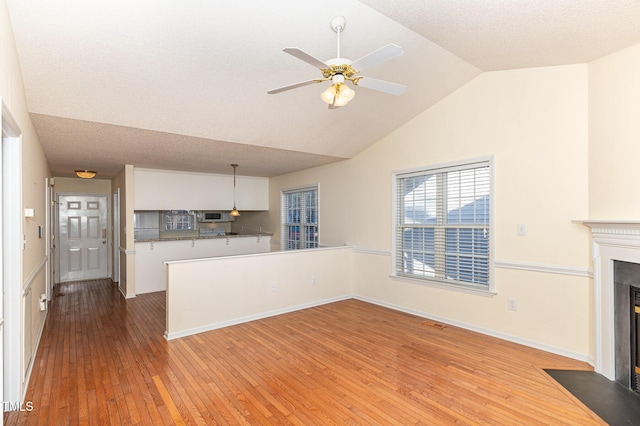 unfurnished living room featuring wood finished floors, a fireplace with flush hearth, a ceiling fan, vaulted ceiling, and baseboards