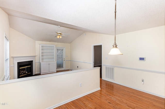 interior space with visible vents, a glass covered fireplace, lofted ceiling, ceiling fan, and wood finished floors