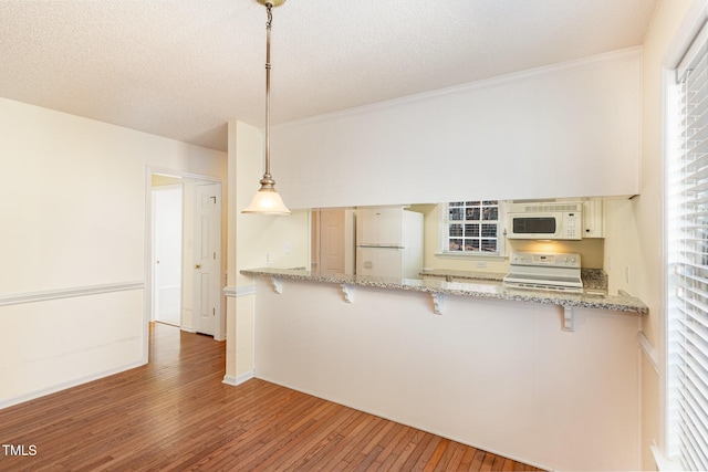 kitchen with white appliances, a kitchen breakfast bar, wood finished floors, hanging light fixtures, and a peninsula