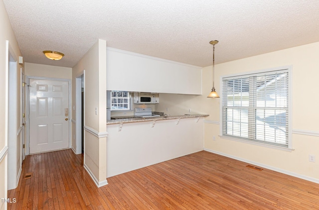 kitchen with visible vents, hanging light fixtures, white cabinets, white appliances, and a peninsula