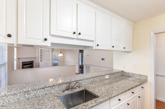 kitchen with a fireplace, light stone counters, white cabinets, and a sink